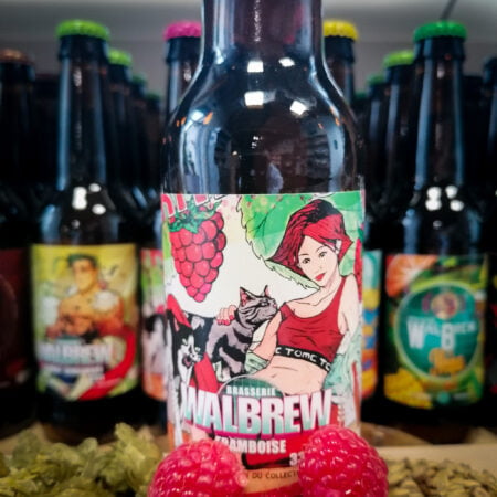 Photo d'une bouteille de bière à la framboise de la brasserie Walbrew, il y a également des framboise au premier plan de cette photo