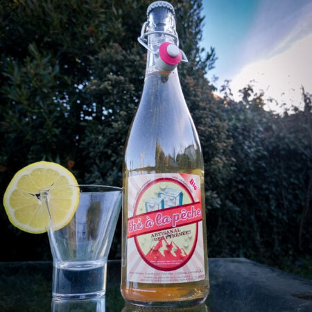 Bouteille en verre de 75cl de thé à la pêche artisanal des pyrénées de la brasserie locale l'aoucataise avec un verre et une tranche de citron