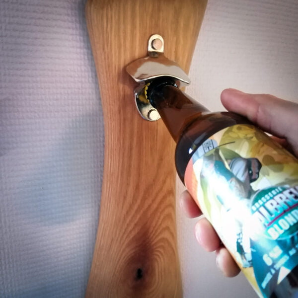 Autre modèle de décapsuleur mural avec une base en bois et l'ouvre bière en métal sur un mur blanc on voit également une bouteille.