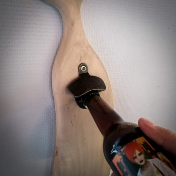 Décapsuleur mural avec une base en bois et l'ouvre bière en métal sur un mur blanc on voit également une bouteille.
