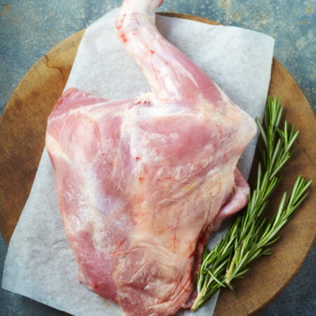 belle épaule de chevreau posée sur du papier cuisson, une planche en bois et des branches de romarin.