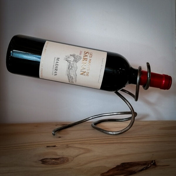 Porte bouteille en métal avec une bouteille de vin Madiran Les Hauts de Sarran de 2016, le tout posé sur une table en bois