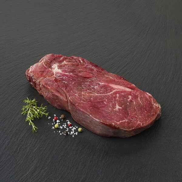 Une très belle basse côte de bœuf posée sur une ardoise noire avec des grains de poivres, du sel et des herbes aromatiques.