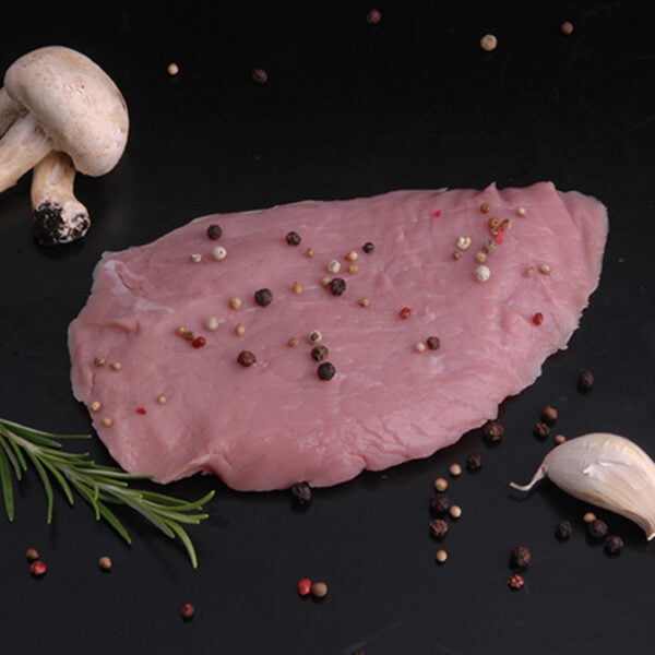 Une escalope de veau sur fond sombre accompagnée de champignons de paris, une gousse d'ail, une branche de romarin et plusieurs grains de poivre ou baies