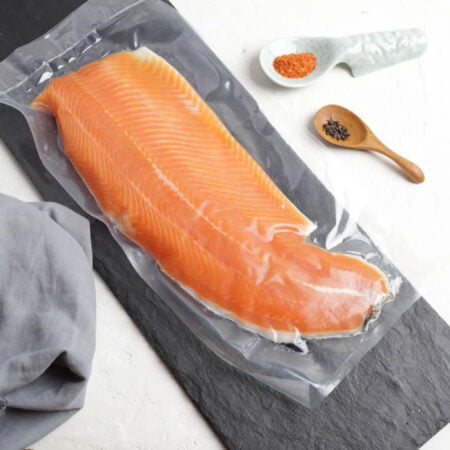 joli filet de truite des pyrénées emballée sous-vide et posé sur une ardoise rectangulaire avec un torchon et 2 cuillères contenant des épices.