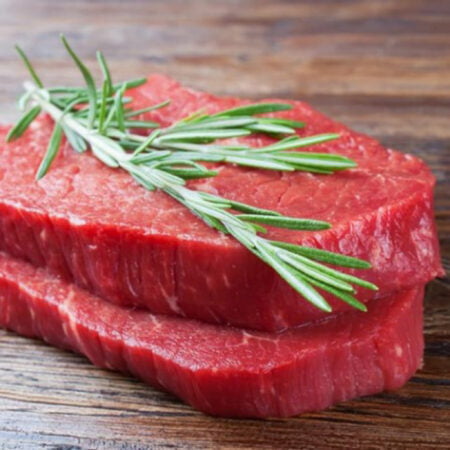 Deux tranches de steak de noix de bœuf empilée sur une planche à découper en bois avec du romarin.