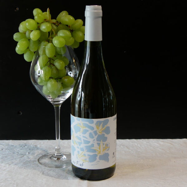 Bouteille de vin blanc lou piaf vue de face avec à coté un verre plein de raisins