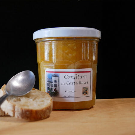 Confiture à l'orange de chez Castelrose sur une planche en bois avec du pain et une cuillère