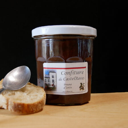 Pot de confiture à la prune d'ente de chez castelrose avec une tranche de pain et une cuillère