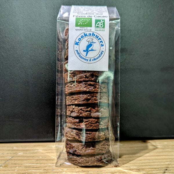 Sur fond noir et sol en bois clair, un paquet transparent de cookies au fèves de Cacao fait par le pâtissier kookaburra