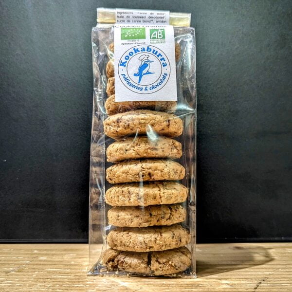 sur cette photo on voit des cookies aux graines dans un emballage plastique transparent et une étiquette kookaburra, le tout sur du bois avec un fond noir mate