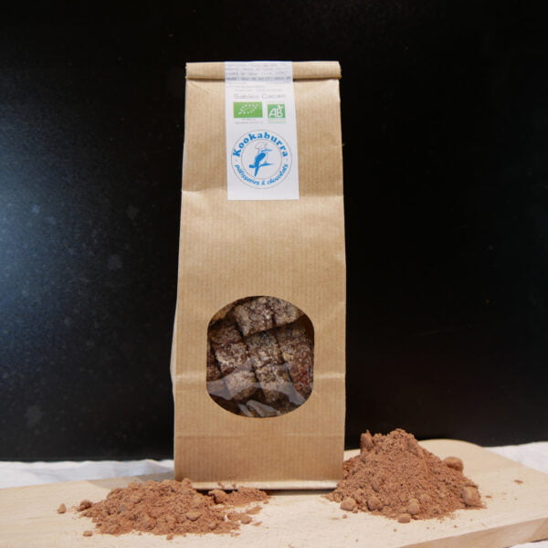 Photo d'un paquet de Sablés au Cacao posé sur une table en bois et produits par Kookaburra dans les Hautes-Pyrénées avec de la poudre de cacao posé devant sur une planche en bois
