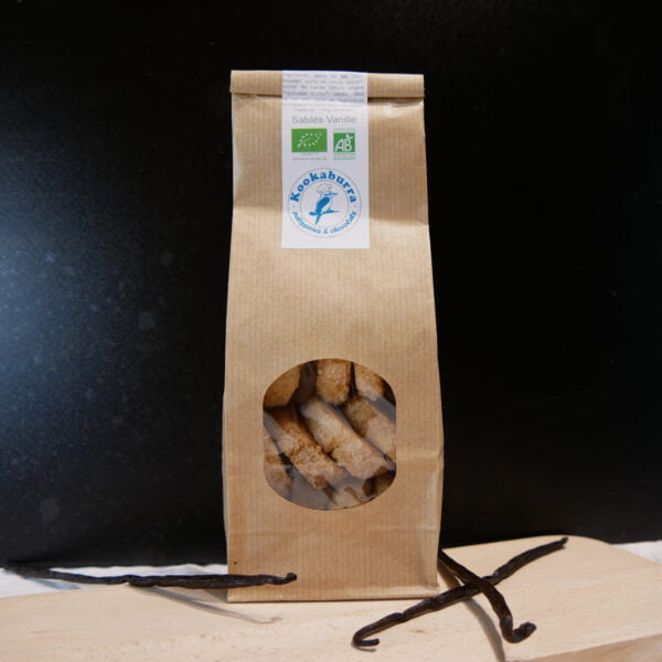 Photo d'un paquet de Sablés au à la vanille posé sur une table en bois et produits par Kookaburra dans les Hautes-Pyrénées posé sur une planche en bois entouré de gousse de vanille