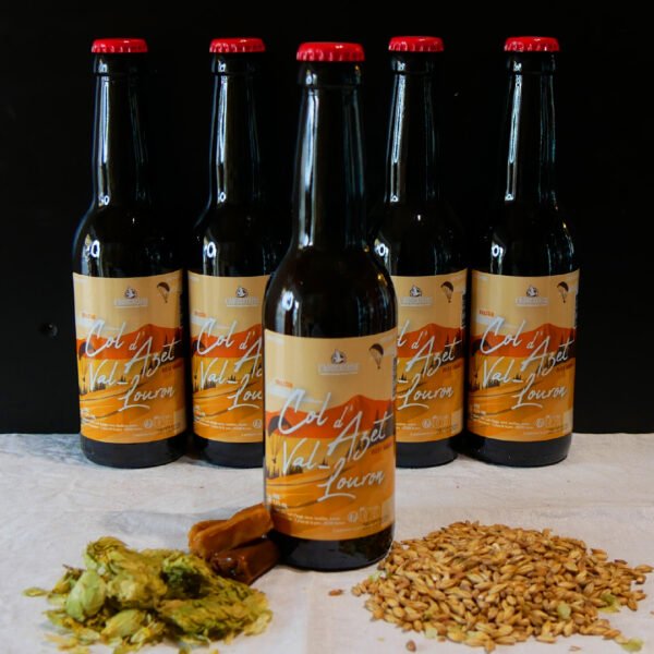 Photo de plusieurs bières avec l'étiquette orange et des morceau de caramel pour accompagné le malt et le houblon à l'avant de l'image