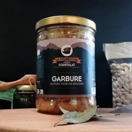 Garbure de 760g au porc noir de bigorre posée sur une planche en bois accompagnée par d'autres produits tel que des haricots Tarbais ou du sel