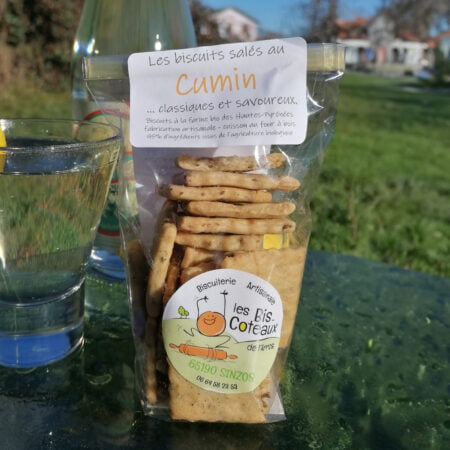 Un sachet de biscuits salés au cumin de la biscuiterie artisanale les Bis-Coteaux d l'Arros basée à Sinzos dans les Hautes-pyrénées. Posé sur une table de jardin en extérieur