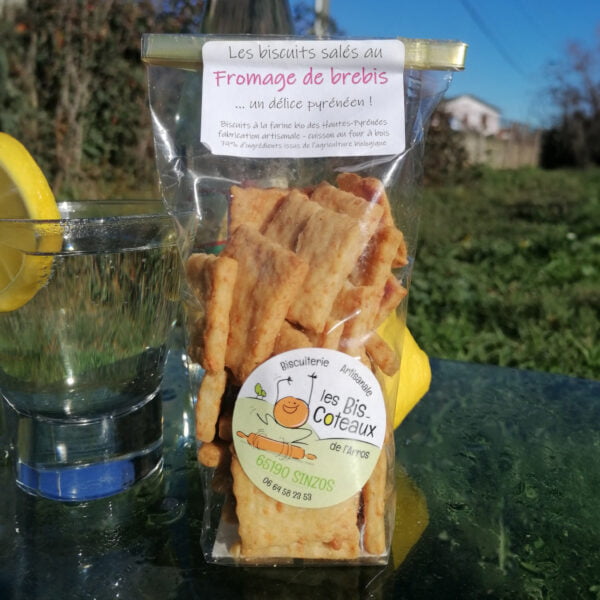sachet de biscuits salés au fromage de brebis de la biscuiterie artisanale les Bis-Coteaux d l'Arros basée à Sinzos dans les Hautes-pyrénées. Posé sur une table de jardin en extérieur avec un verre d'eau et une rondelle de citron