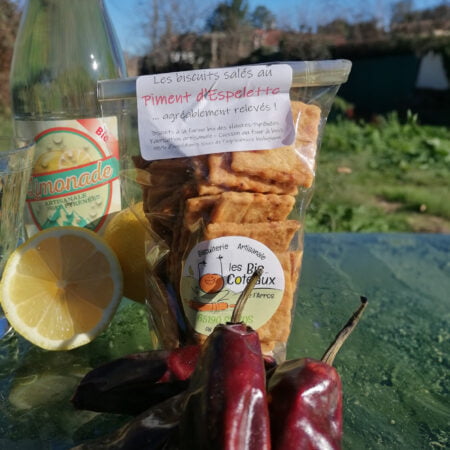 Paquet de biscuits salés au piment d'Espelette agréablement relevés, de la biscuiterie les Bis-Coteaux de l'Arros posé sur une table avec une bouteille de limonade au citron