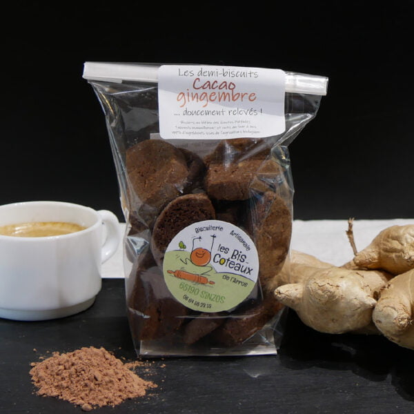 Photo d'un sachet de demi-biscuits cacao gimgembre posé sur une planche en bois avec du cacao et du gingembre . Produits par la Biscuiterie Artisanale Les Bis-Coteaux de l'Arros à Sinzos dans les Hautes-Pyrénées.