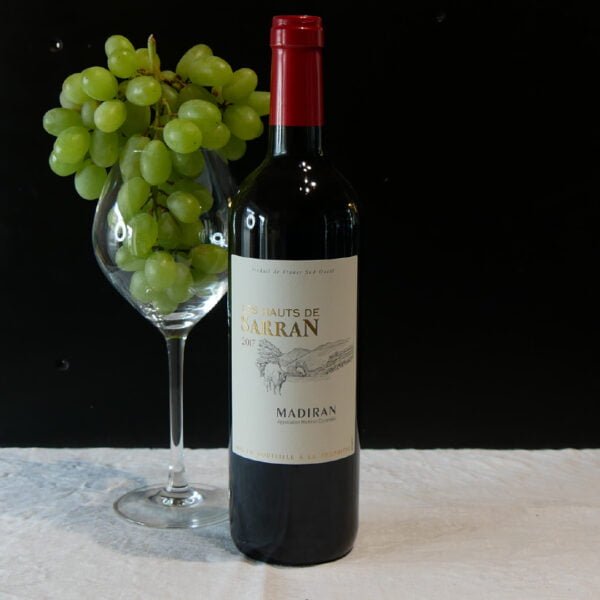 Bouteille de vin rouge les hauts de sarran madiran 2017 accompagnée par un verre de vin et de raisin
