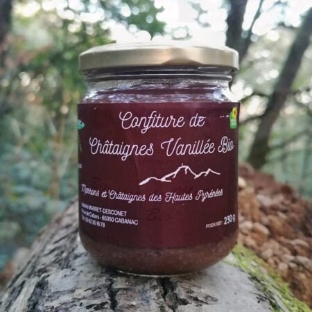 Photo d'un pot de Confiture de Châtaignes Vanillée Bio posé sur un tronc d'arbre dans une forêt. c'est un pot de 230g