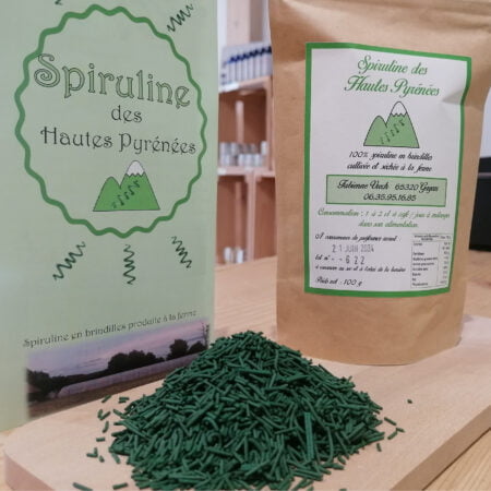 Photo d'un paquet de Spiruline des Hautes-Pyrénées en brindilles cultivée et séchée à la ferme à Gayan posé sur une planche en bois sur laquelle est également posé un tas de spiruline