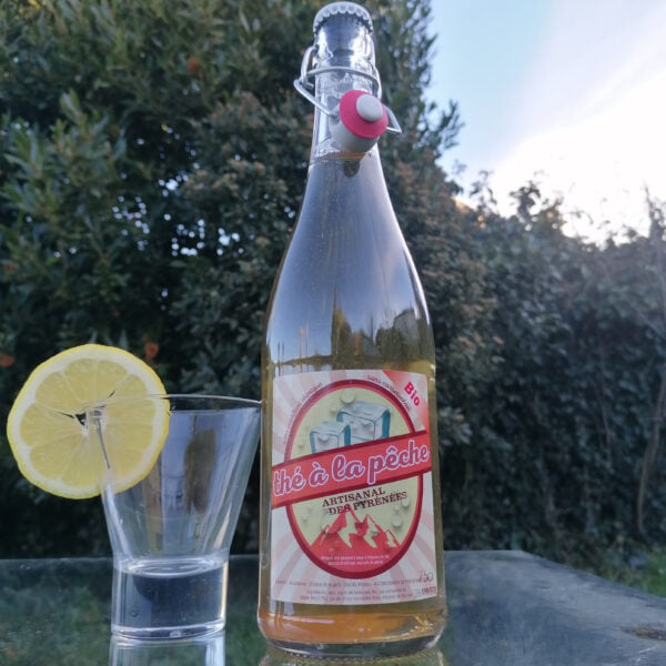 Bouteille en verre de 75cl de thé à la pêche artisanal des pyrénées de la brasserie locale l'aoucataise avec un verre et une tranche de citron