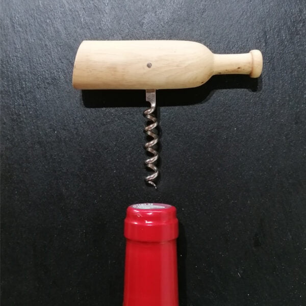 Vue de dessus d'un tire-bouchon en bois, taillé en forme de bouteille de vin, on voit également le goulot rouge d'une bouteille de vin sur le bas de la photo, le tout est posé sur une ardoise noire.