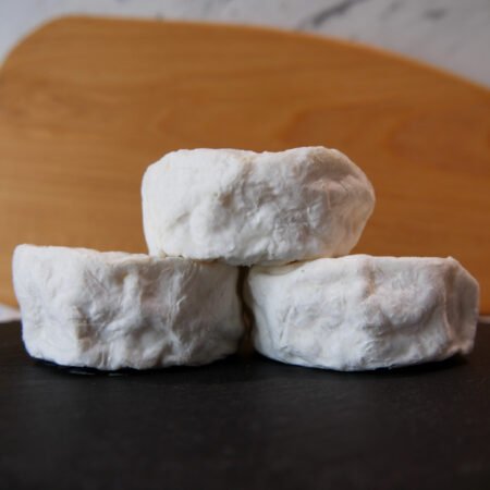 Trois petits palets de fromage de vache posés les uns sur les autres devant une planche en bois