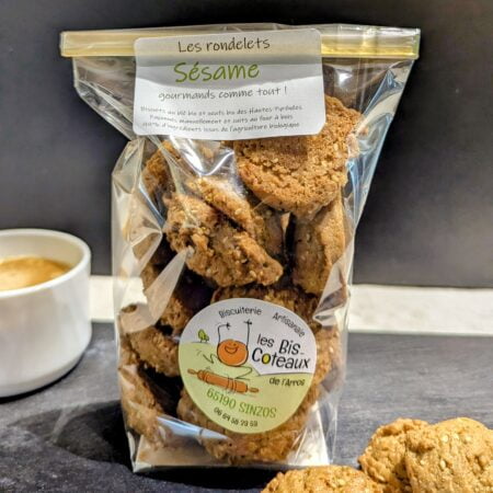 Paquet de biscuits au sésame du producteur les Bis-Coteaux sur une adroise noire, en premier plan des biscuits au sésame, en arrière plan une tasse à café le tout sur un fond noir