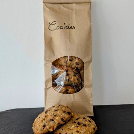 2 cookies de la Ferme Soubiren, devant un paquet remplis de ces fameux cookies. Le tout posé sur une ardoise noire, devant un fond blanc