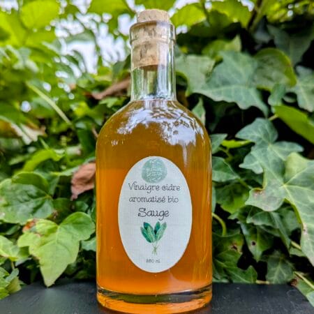 de la végétation, lierre, en fond, devant laquelle trone une bouteille de vinaigre de cidre aromatisé à la sauge