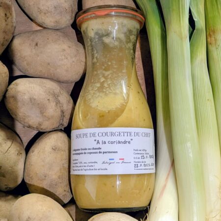 Une bouteille de soupe à la courgette et coriandre posée sur un tas de légumes