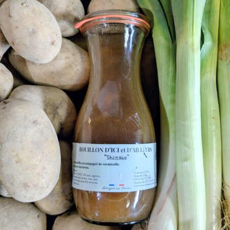 Un tas de pommes de terre et de poireaux sur lequel est posée une bouteille de bouillon de shiitakés