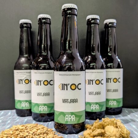 photo représentant les bières Américan Pale Ale (APA) de chez In'Oc au centre, devant un fond noir et derrière des tas de malts et de houblon